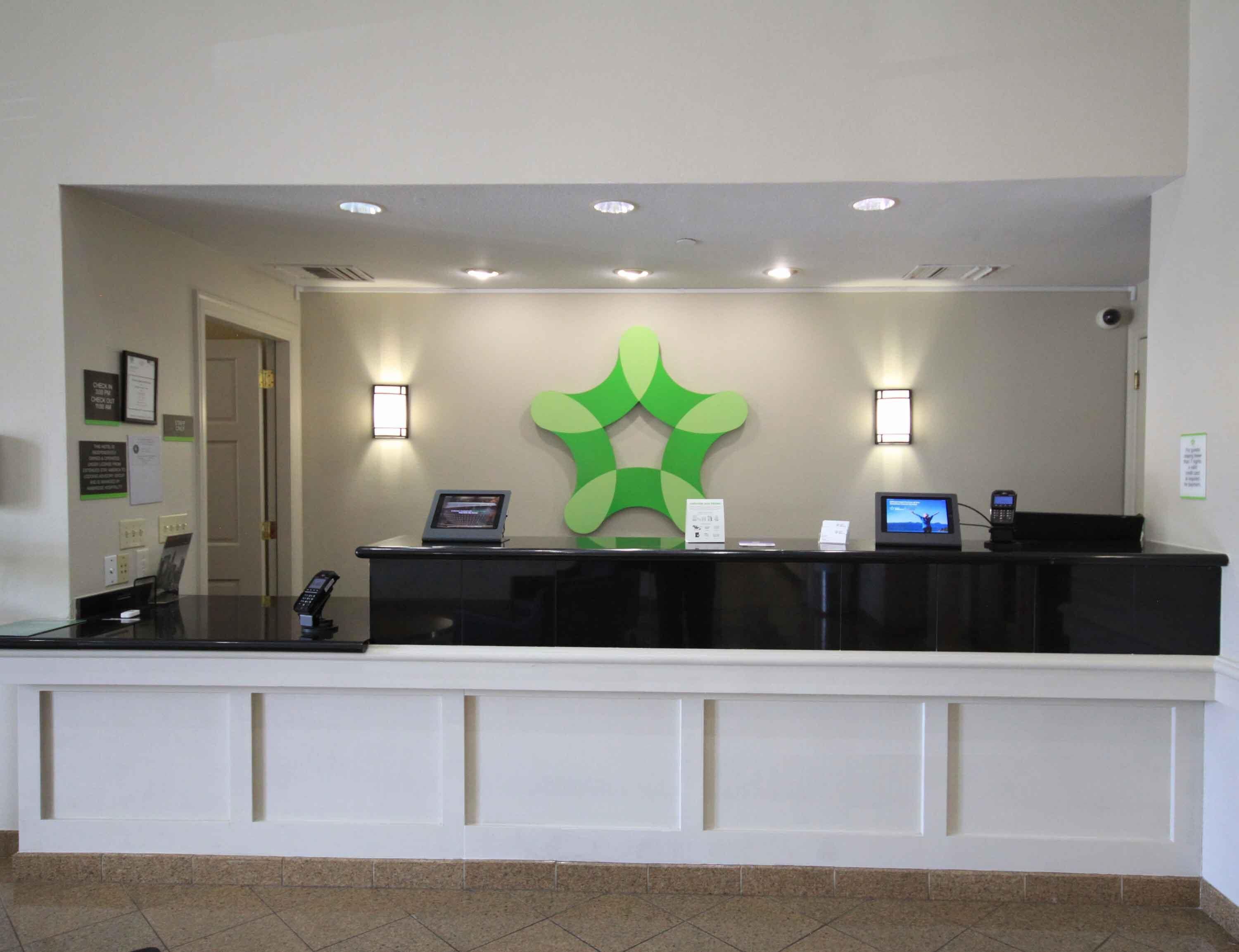 A reception desk with a green logo, a computer, a phone, and a small screen.