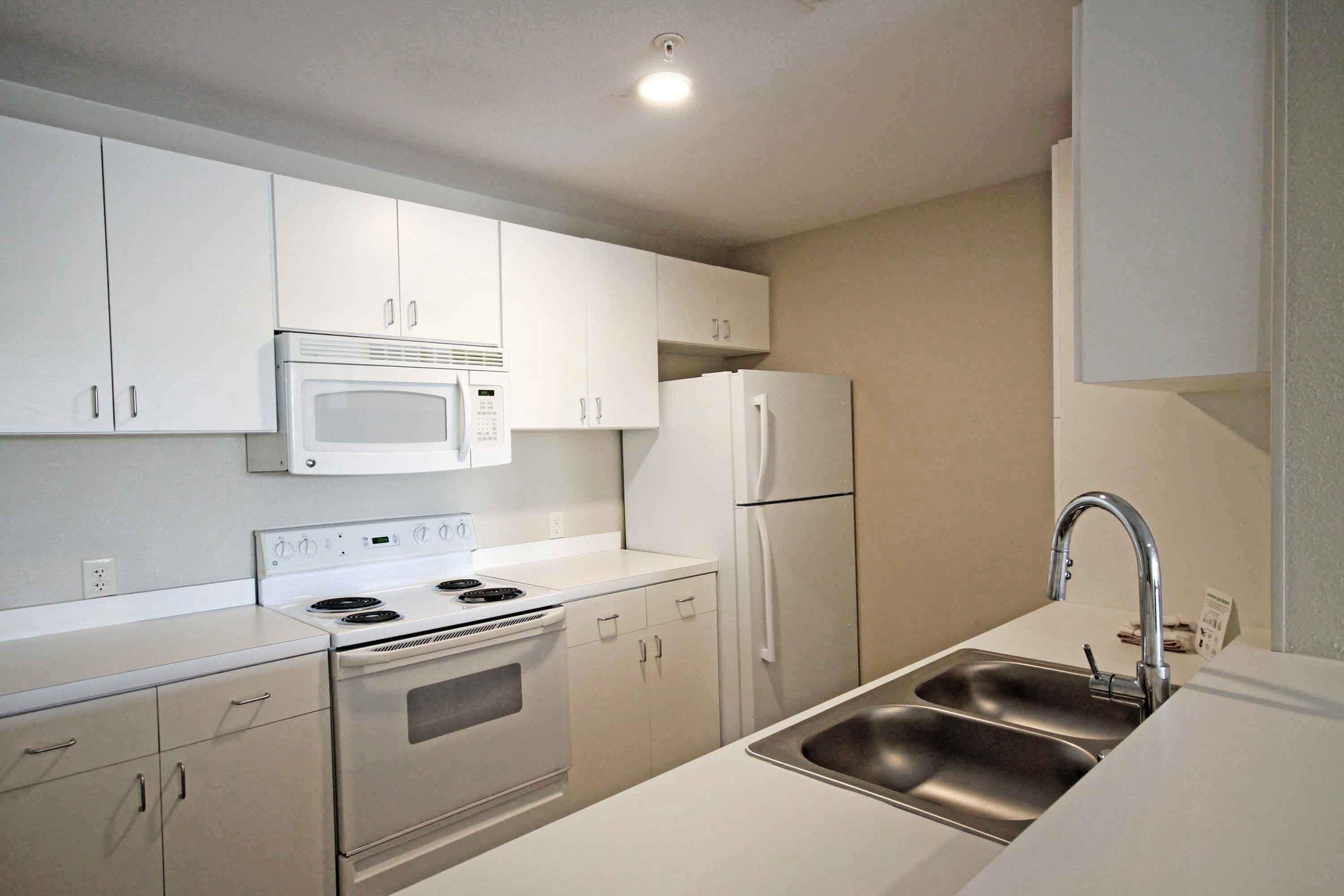 A modern kitchen with white cabinets, a stainless steel sink, a microwave, a refrigerator, and an oven.