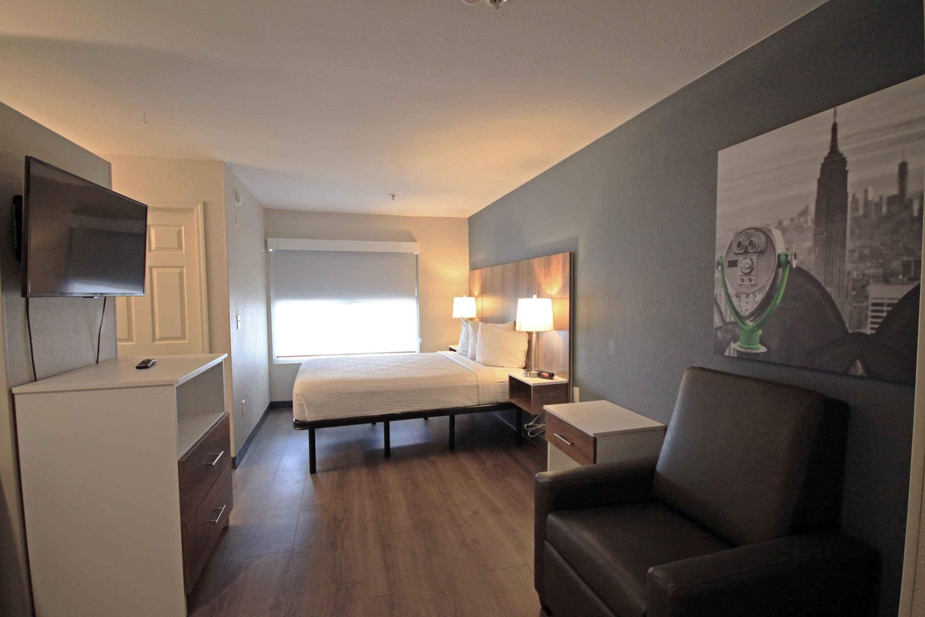 Una camera d'albergo con un letto, comodini, una TV, una poltrona e un quadro appeso al muro.