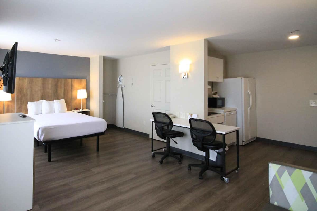A hotel room with a bed, desk, two chairs, a refrigerator, a microwave, a TV, and a hairdryer.