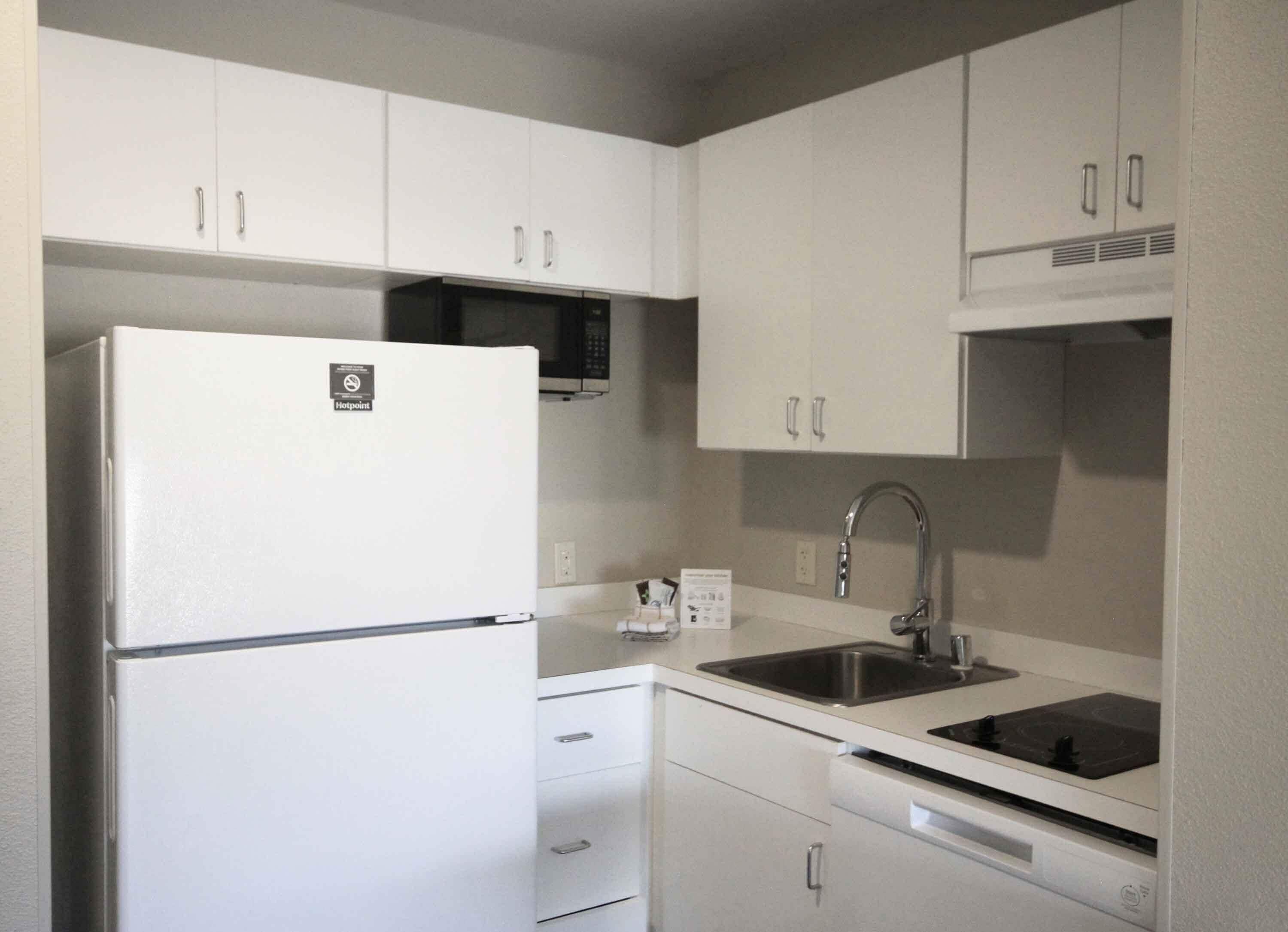 A compact kitchen with white cabinets, a built-in microwave, a stainless steel sink, and a dishwasher.