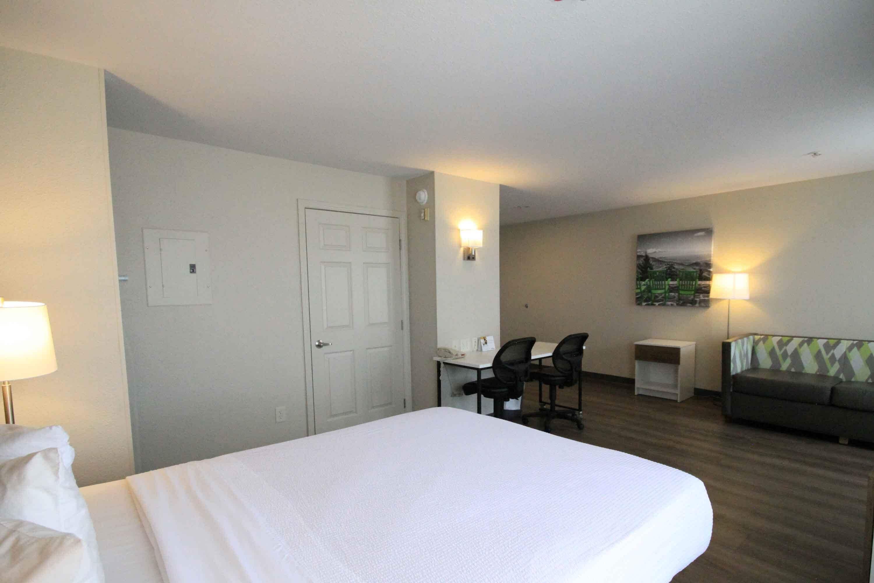 Une chambre d’hôtel comprenant un lit, un bureau avec deux chaises, une petite table, un canapé et un tableau au mur.