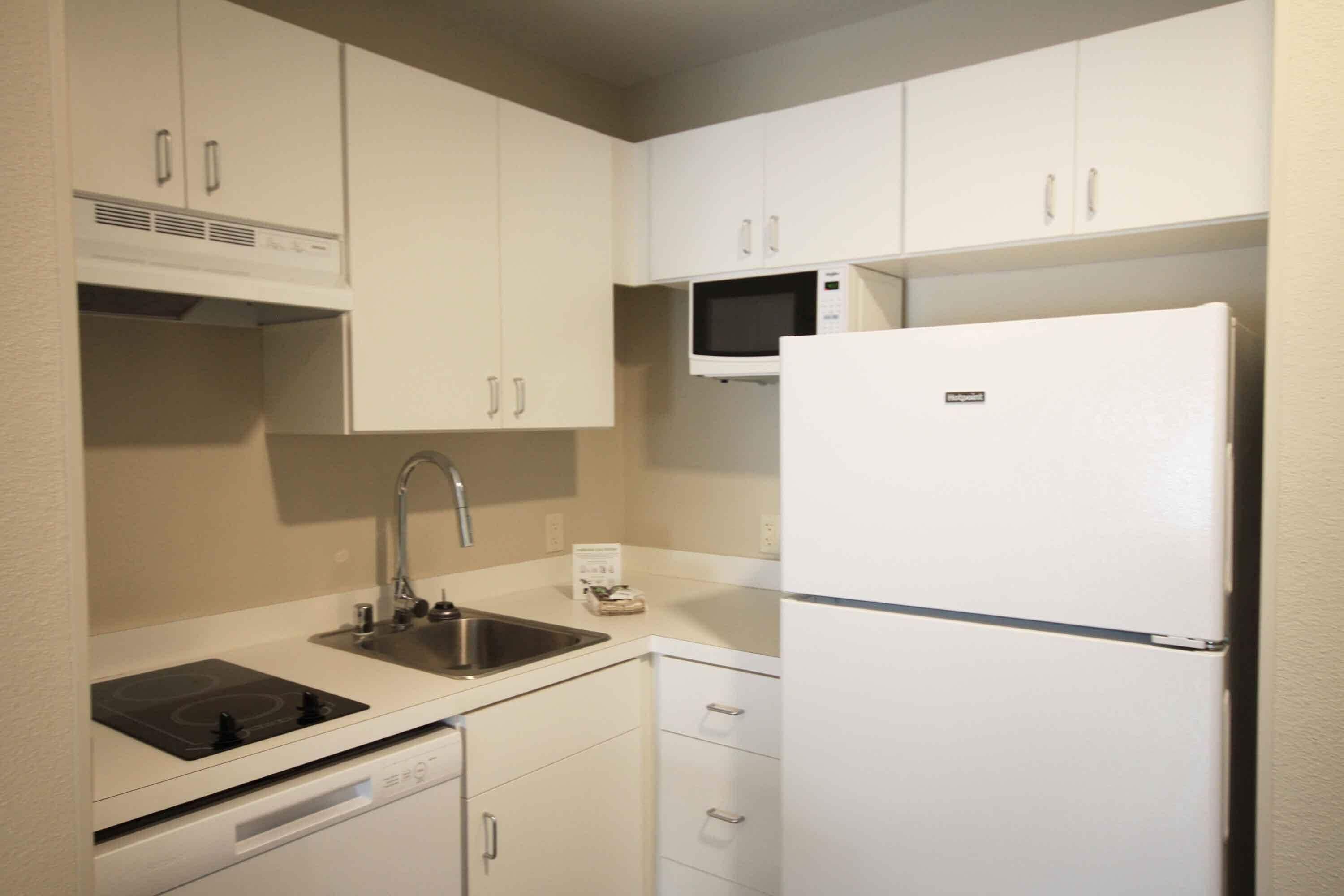 A compact kitchen with white cabinets, a built-in microwave, a stainless steel sink, and a dishwasher.