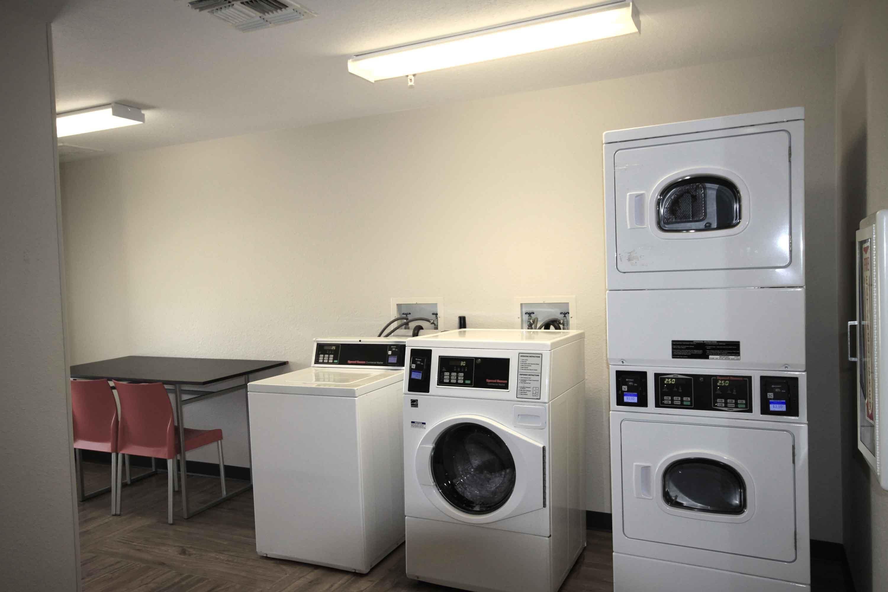 A laundry room with two stacked washing machines, a table, and two chairs.