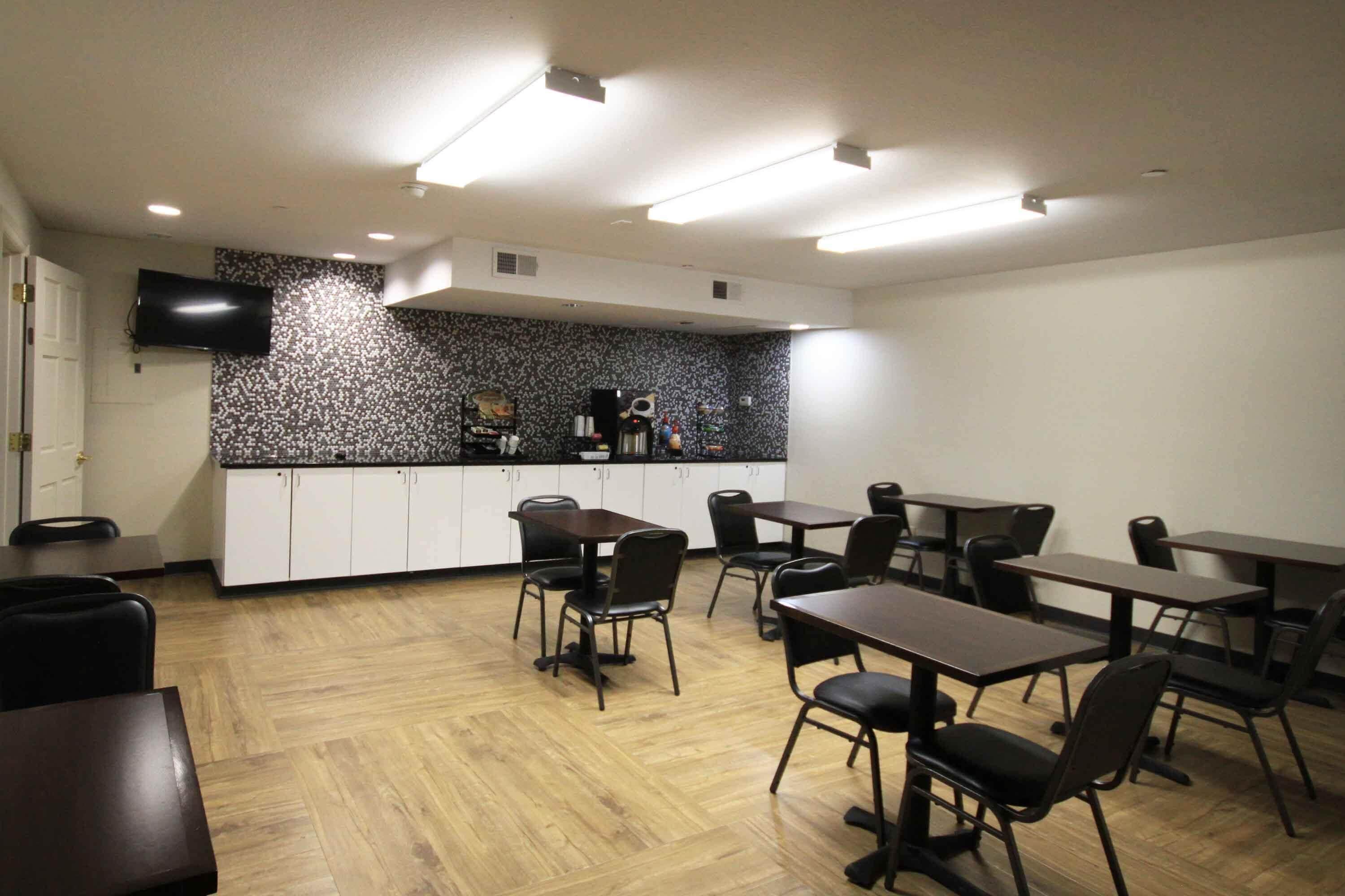 Ein Konferenzraum mit Tischen, Stühlen, einer Küchenzeile und einem an der Wand montierten Flachbildfernseher.