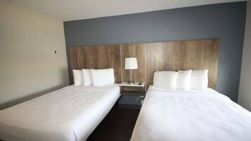 A hotel room with two single beds, a wooden headboard, a nightstand with a lamp, and a small table.