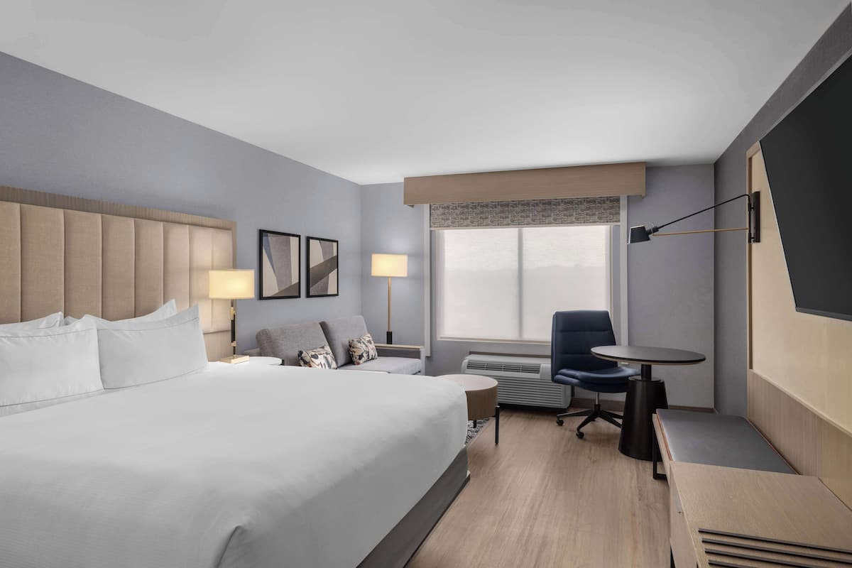 Una habitación de hotel moderna con una cama grande, un escritorio, una silla, una mesita y una ventana con vistas.