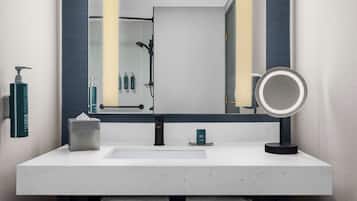 Un baño moderno con un lavamanos blanco, un espejo grande y un cabezal de ducha de mano.