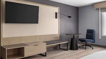 Una habitación de hotel moderna con televisión integrada, un escritorio, una silla y una mesita.