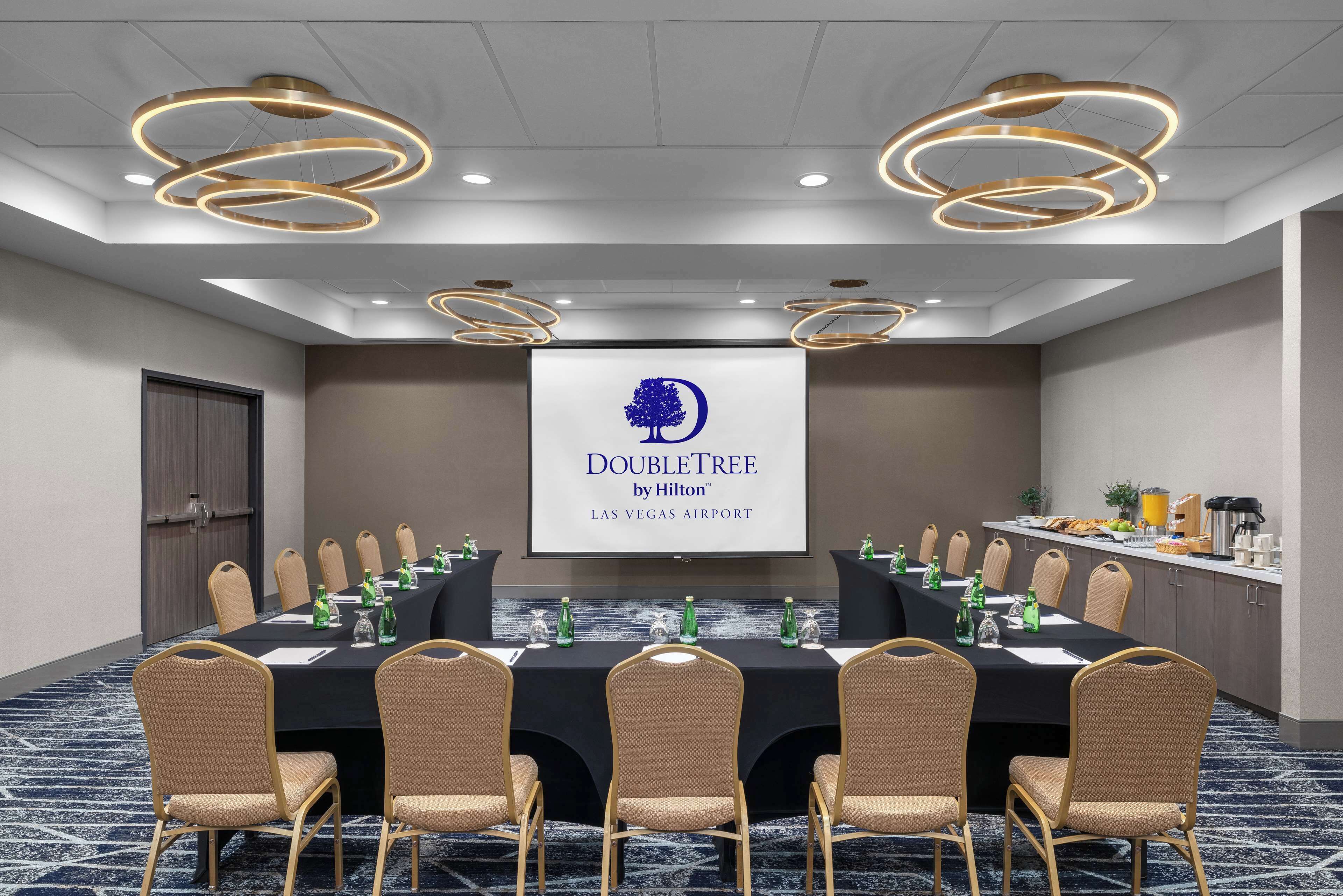 Une salle de conférence avec une longue table, des chaises de couleur beige et un écran affichant le logo de la chaîne DoubleTree by Hilton.