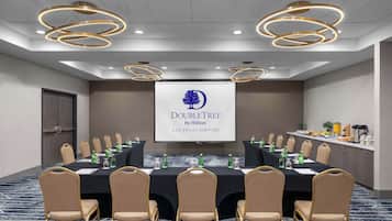 Una sala de conferencias con una mesa larga, sillas color beige y una pantalla que muestra el logo de DoubleTree by Hilton.