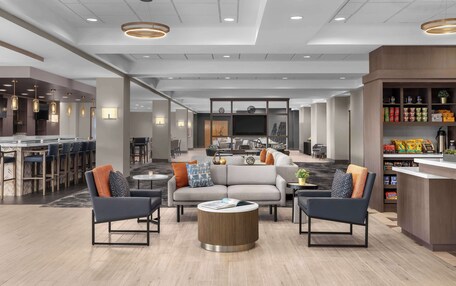 A modern hotel lobby with a seating area, a bar, and a kitchenette.