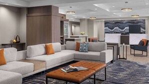 Eine moderne Hotelhalle mit einer Eckcouch, einem Couchtisch und einem großen, abstrakten Wandbild.