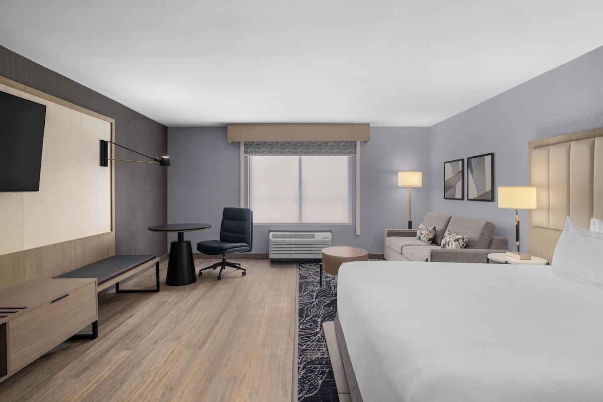 Habitación de hotel moderna con cama, escritorio, silla, sofá, televisor y ventana.