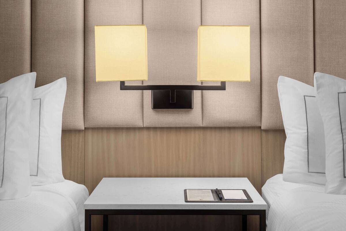 Una habitación de hotel con una cama, dos mesitas de noche y una lámpara de pared.