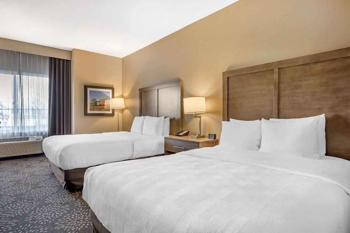 Ein Hotelzimmer mit zwei Betten, einem großen Fenster mit Vorhängen, einem Gemälde an der Wand und Nachttischlampen.