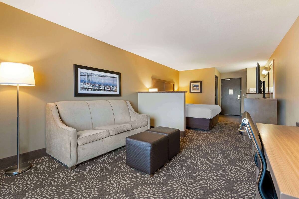 Ein Hotelzimmer mit Sofa, Hocker und einem Bett. Es gibt einen Schreibtisch mit Spiegel und Lampe.