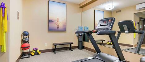 Gimnasio de hotel con cinta de correr, pesas y banco.