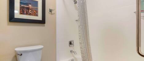 Ein Badezimmer mit Toilette, einem gerahmten Bild an der Wand, einer Badewanne und einer Duschvorhang.