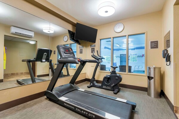 Un gimnasio con cintas de correr, una bicicleta estática y un espejo grande.