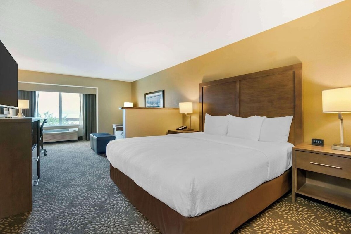Habitación de hotel con una cama grande, un escritorio, una silla, una lámpara, un teléfono y una ventana.