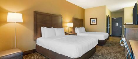A hotel room with two beds, a desk, a lamp, and a patterned carpet.
