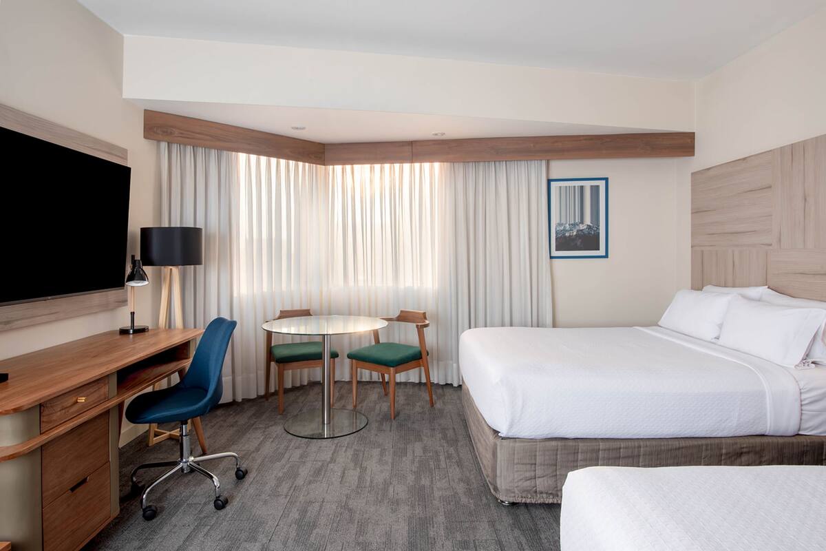 A hotel room with a bed, a desk, a chair, a table, and a TV.