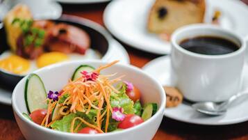 A dining table with a salad bowl, a cup of coffee, and plates with food.