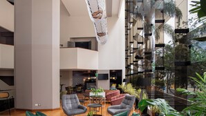 A spacious lobby with modern furniture, a dining area, and a large glass wall offering a view of the outdoors. - Crowne Plaza Lima - Miraflores by IHG (Lima)