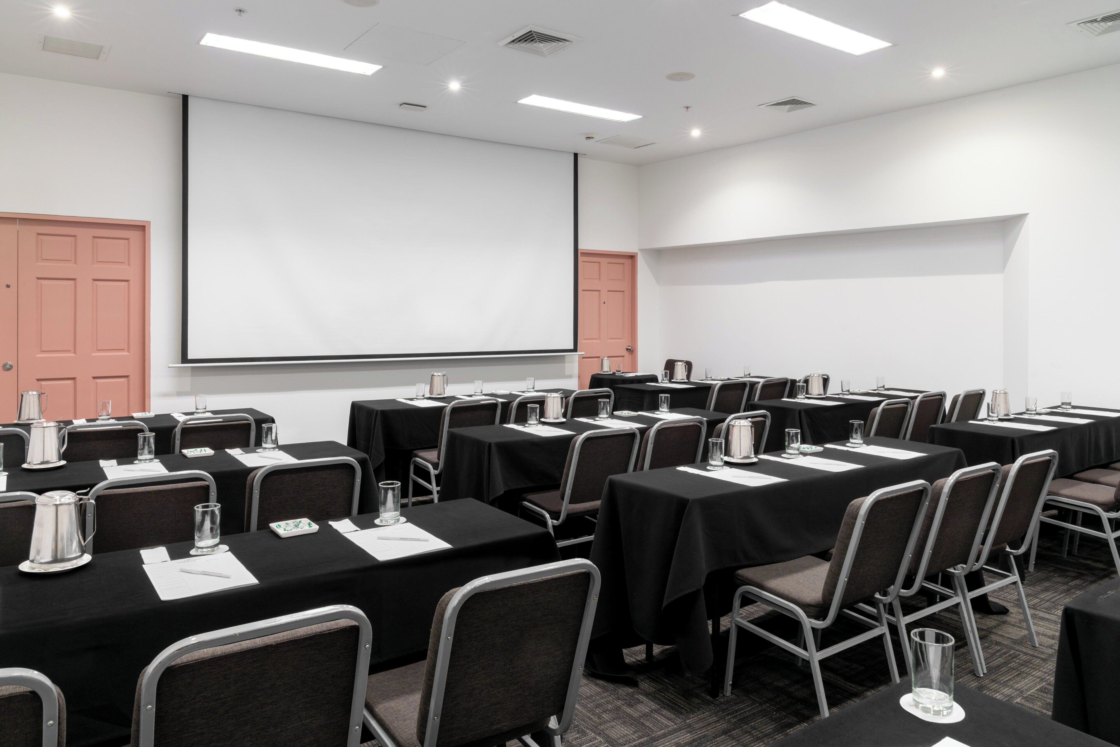 Een vergaderzaal met meerdere tafels, stoelen, een projectiescherm en een whiteboard.