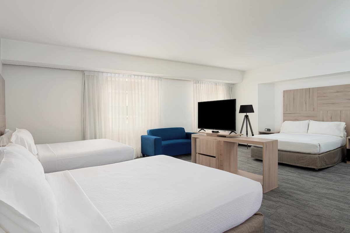 A hotel room with two beds, a desk with a TV, a chair, and a lamp.