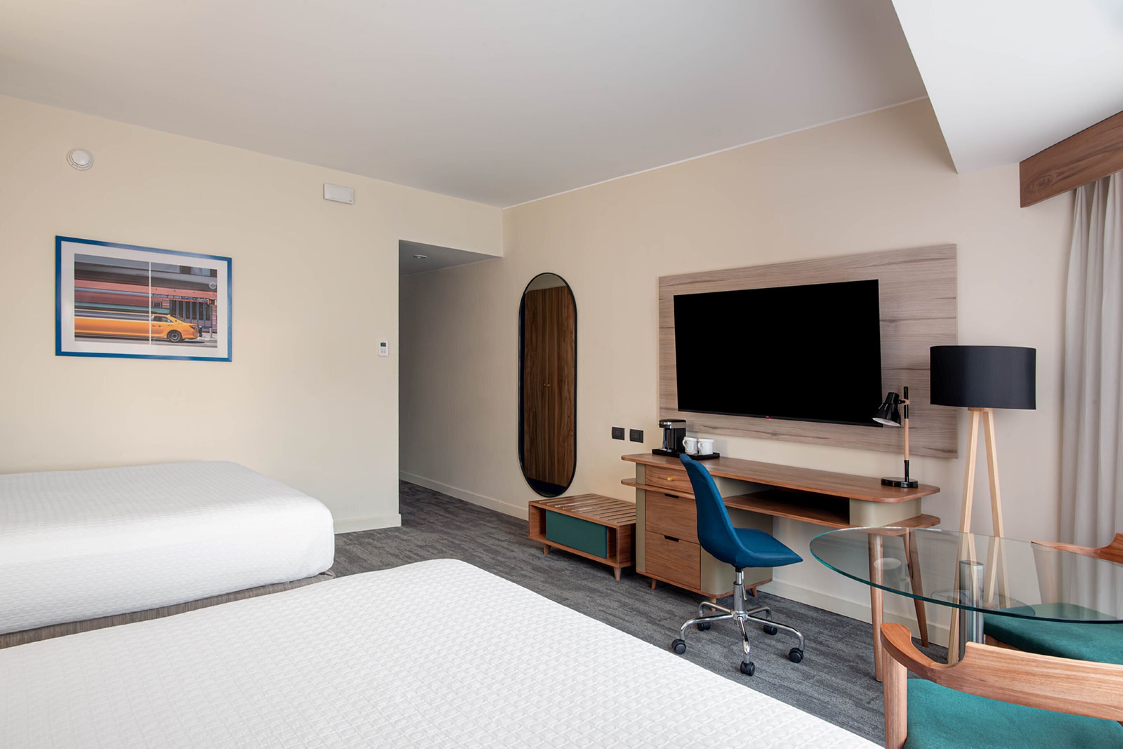 A hotel room with two beds, a desk, a chair, a TV, and a mirror.