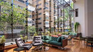 A modern living room with a green sofa, two armchairs, and a coffee table. There are potted plants and a large window offering a view of a building and trees. - Crowne Plaza Lima - Miraflores by IHG (Lima)