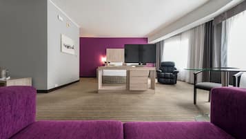 A modern hotel room with a bed, a desk, a TV, and two chairs.