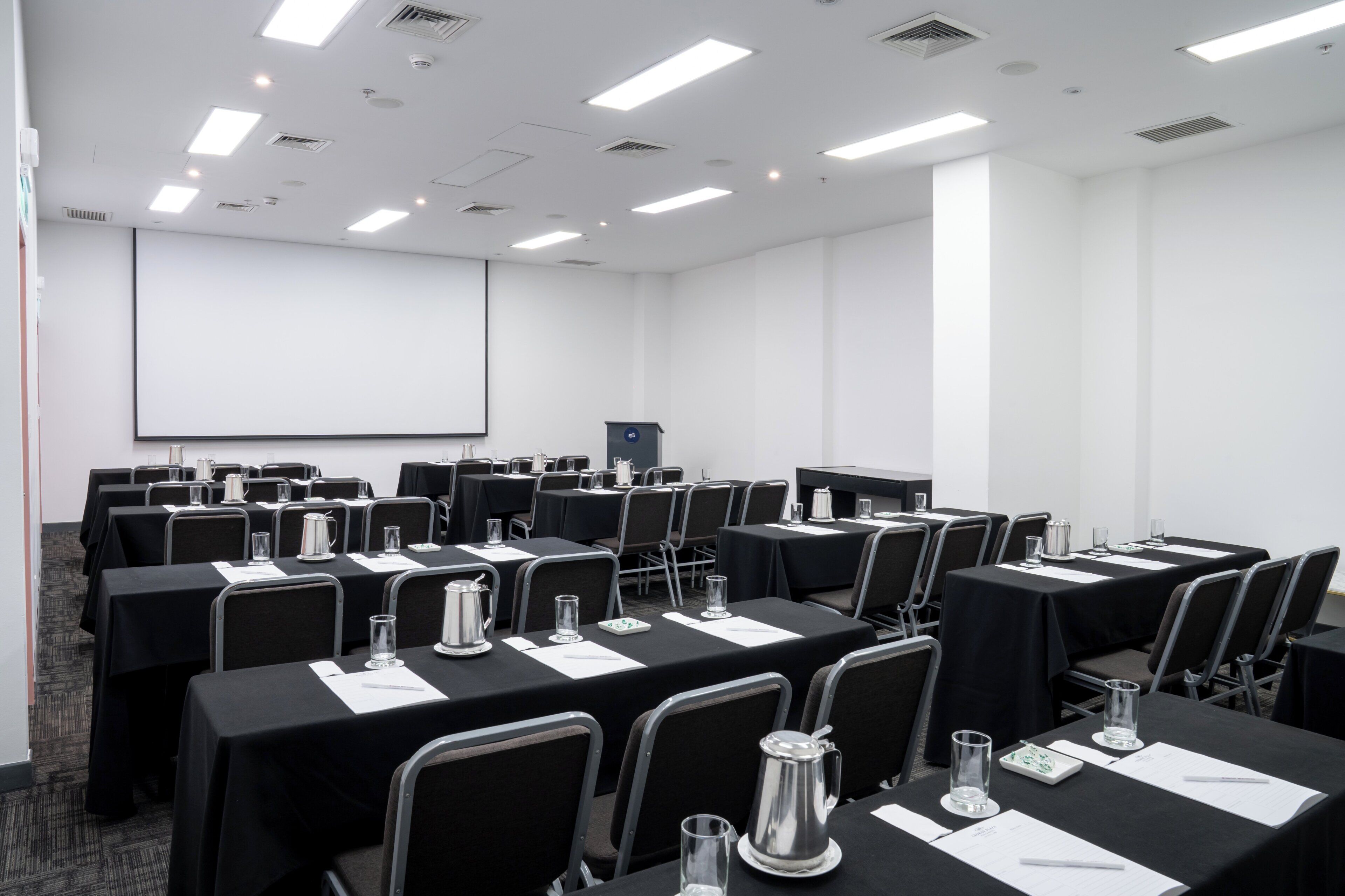 Une salle de conférence équipée de plusieurs tables, de chaises et d’un écran de projection.