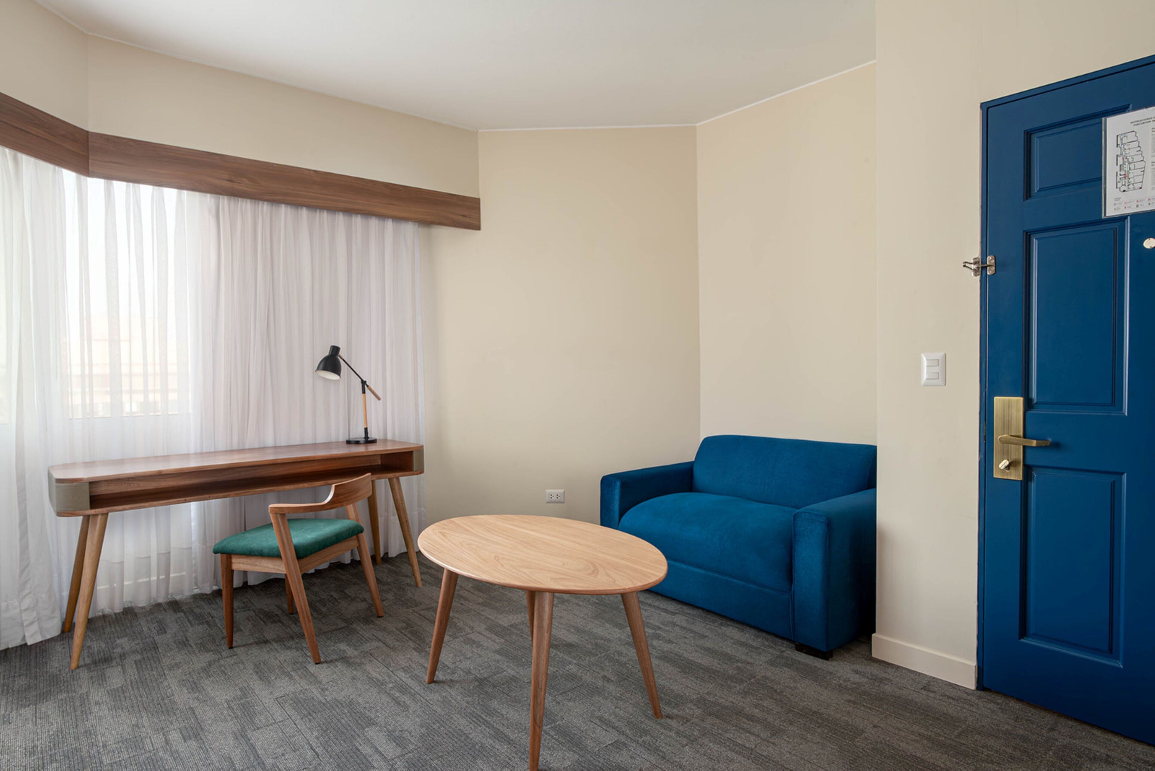 Ein Zimmer mit Schreibtisch, Stuhl, rundem Tisch, blauem Sofa und einer blauen Tür.