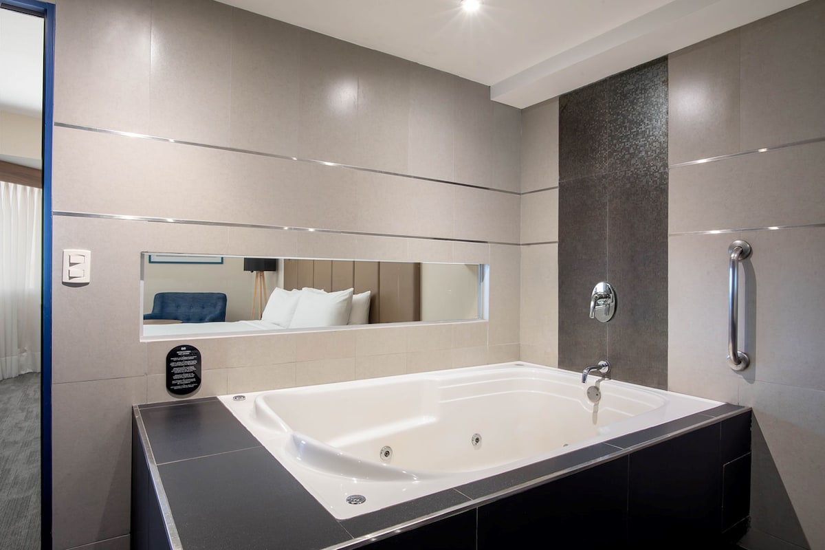 A modern bathroom with a large bathtub, a mirror, and a handrail.