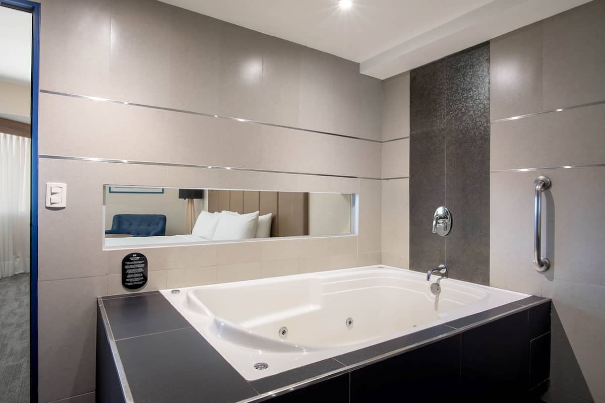 A modern bathroom with a large bathtub, a mirror, and a handrail.