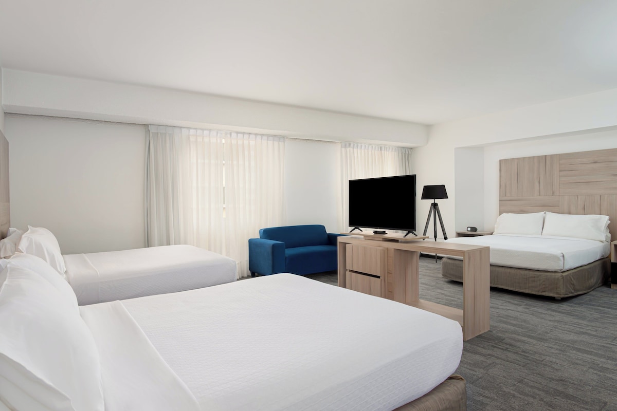 A hotel room with two beds, a desk with a TV, a chair, and a lamp.