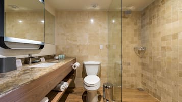 A modern bathroom with a marble countertop, a toilet, a glass shower enclosure, and a trash can.