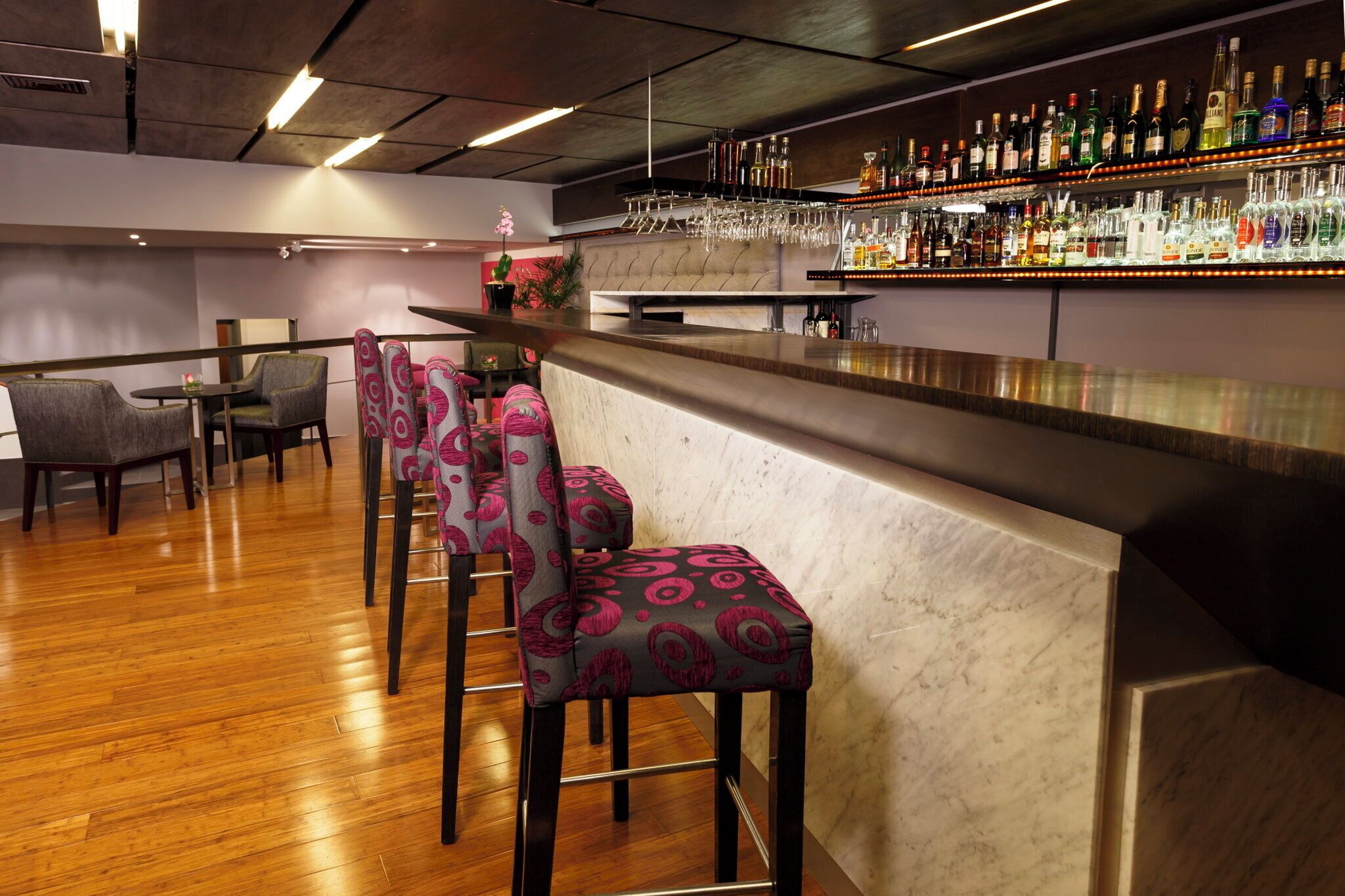 A bar area with a marble counter, multiple liquor bottles, and bar stools with patterned upholstery.