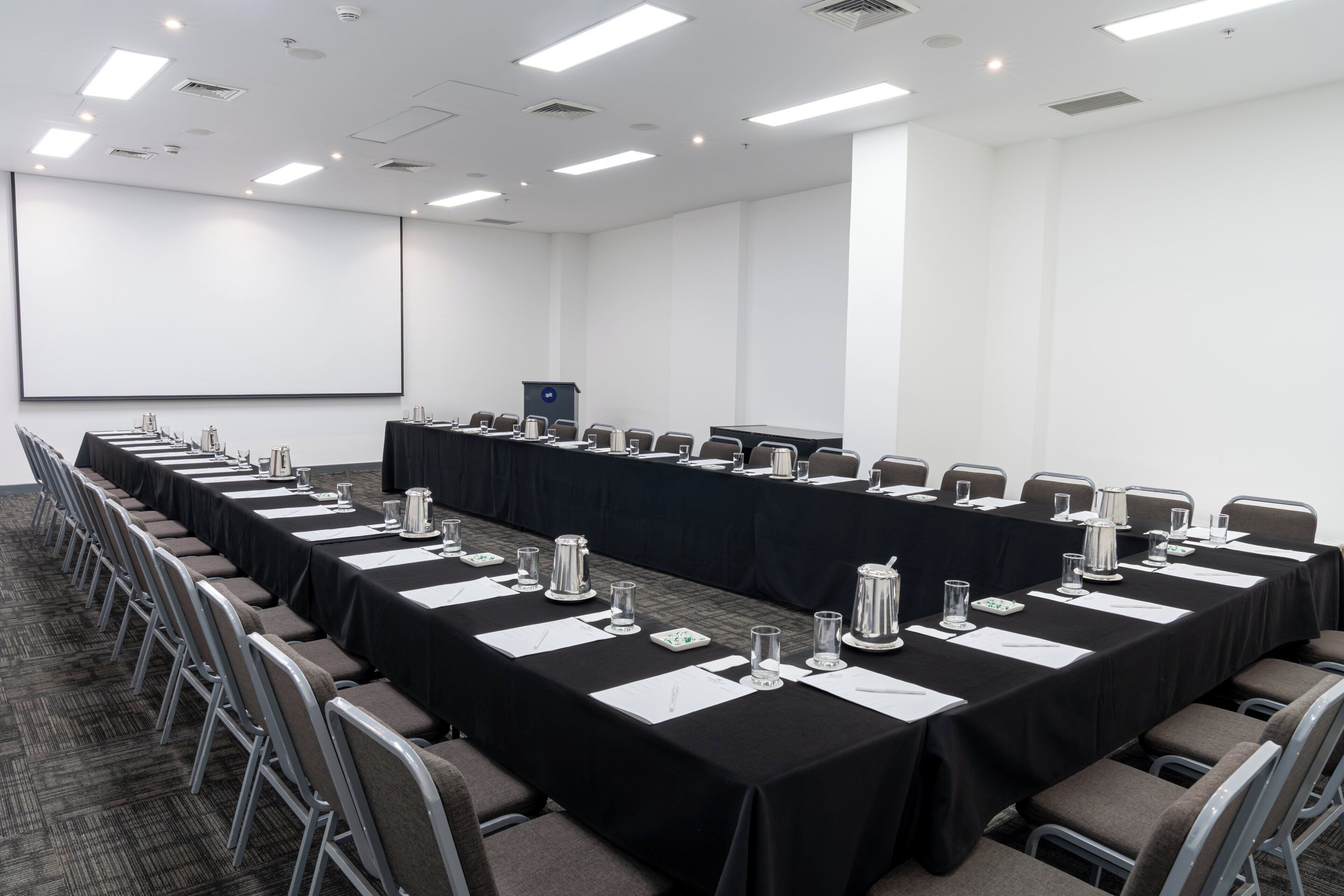A conference room with a long table, chairs, a projector screen, and a podium.