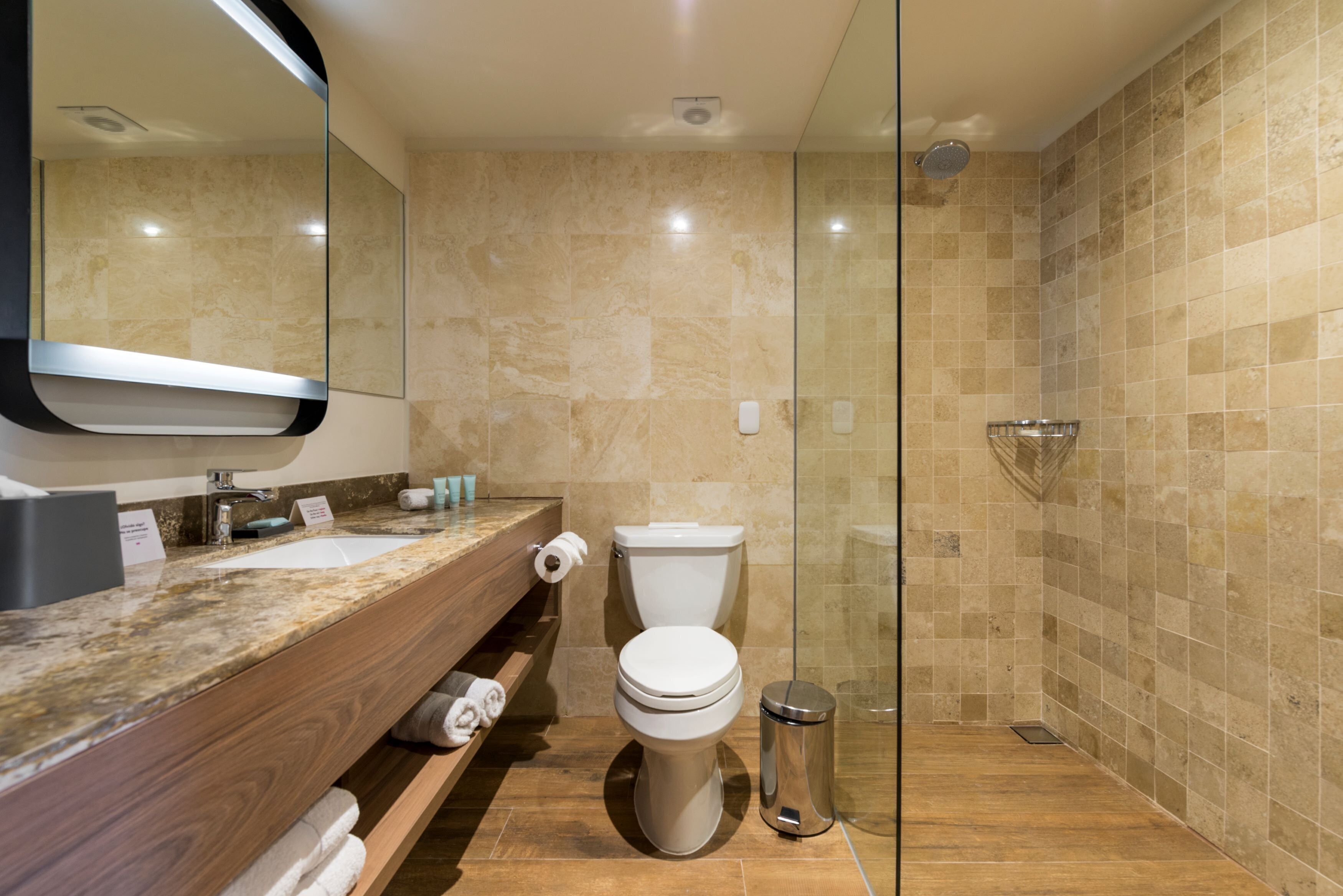 Un baño moderno con encimera de mármol, inodoro, cabina de ducha de cristal y cubo de basura.