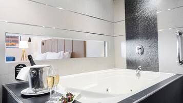 A modern bathroom with a large bathtub, a mirror, and a countertop with a kettle, glasses, and chocolate-covered strawberries.
