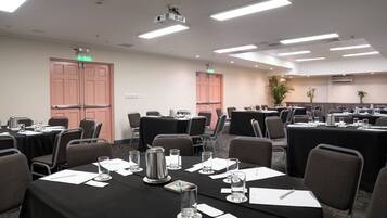 Un salón de conferencias con varias mesas, sillas y un proyector.
