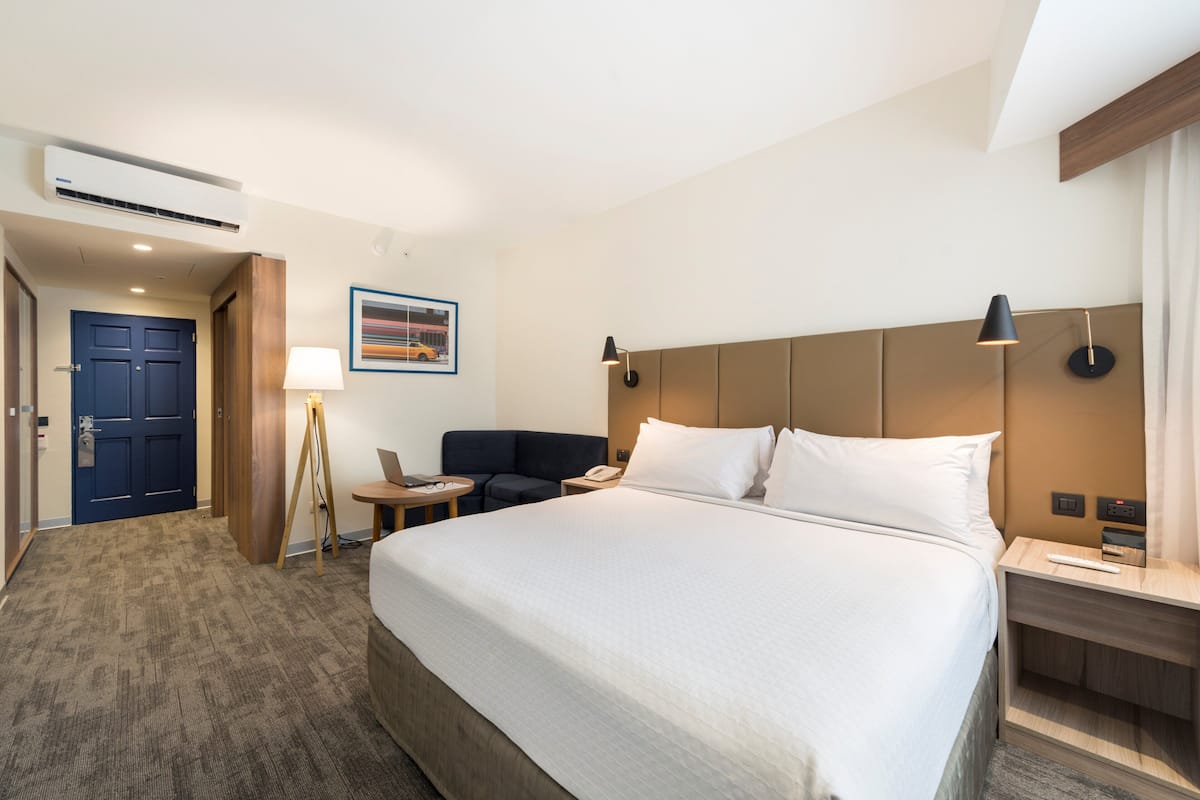 A hotel room with a large bed, a desk, a chair, a lamp, and a painting on the wall.