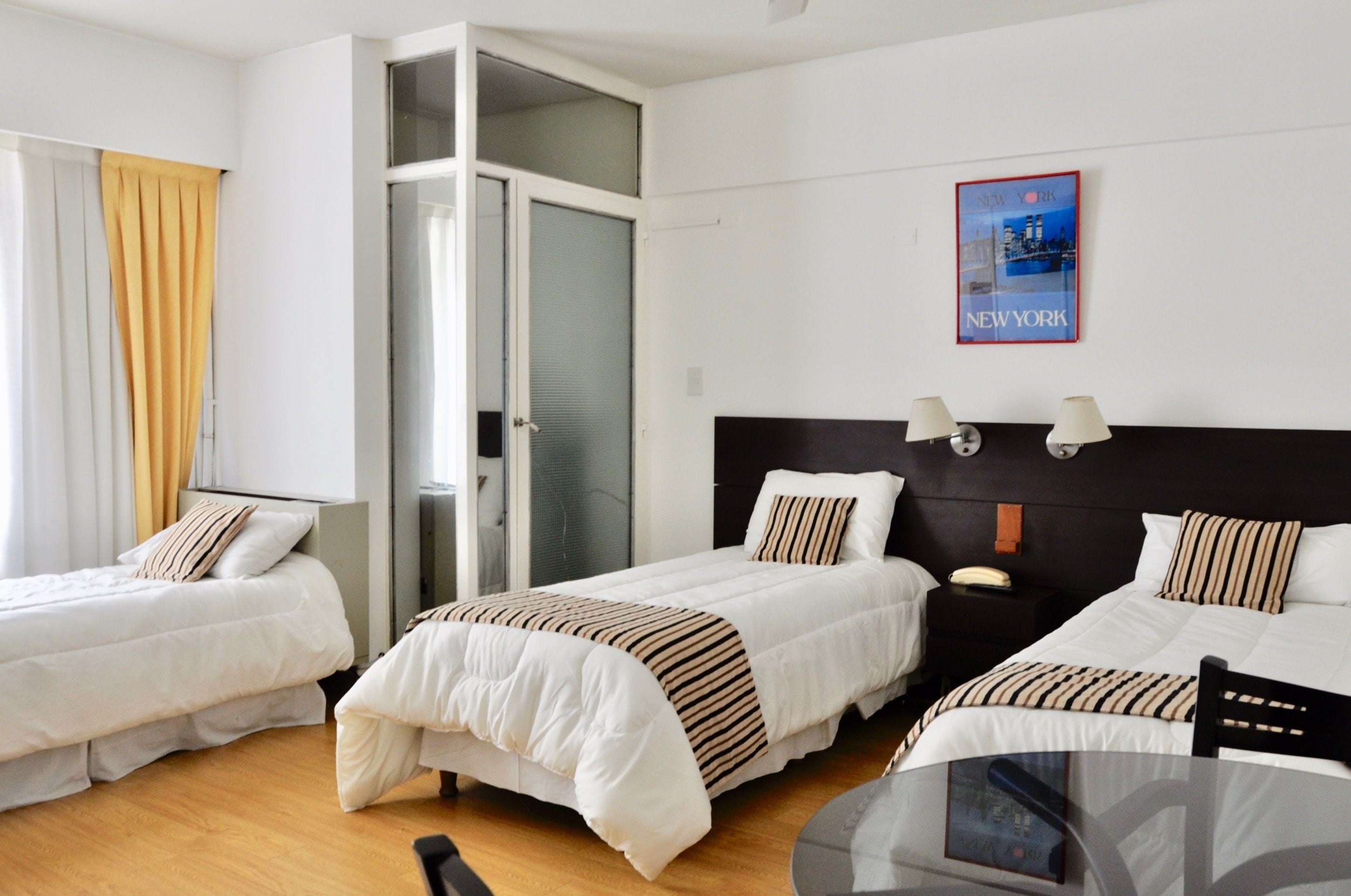 A hotel room with two single beds, a small table, and a poster of New York City.