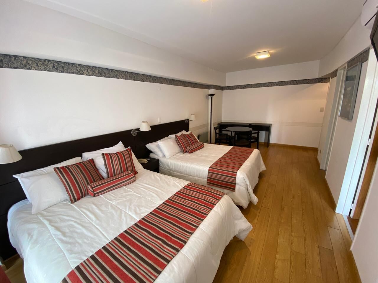 A hotel room with two beds, each with striped bedding and pillows, a small table, and a lamp.