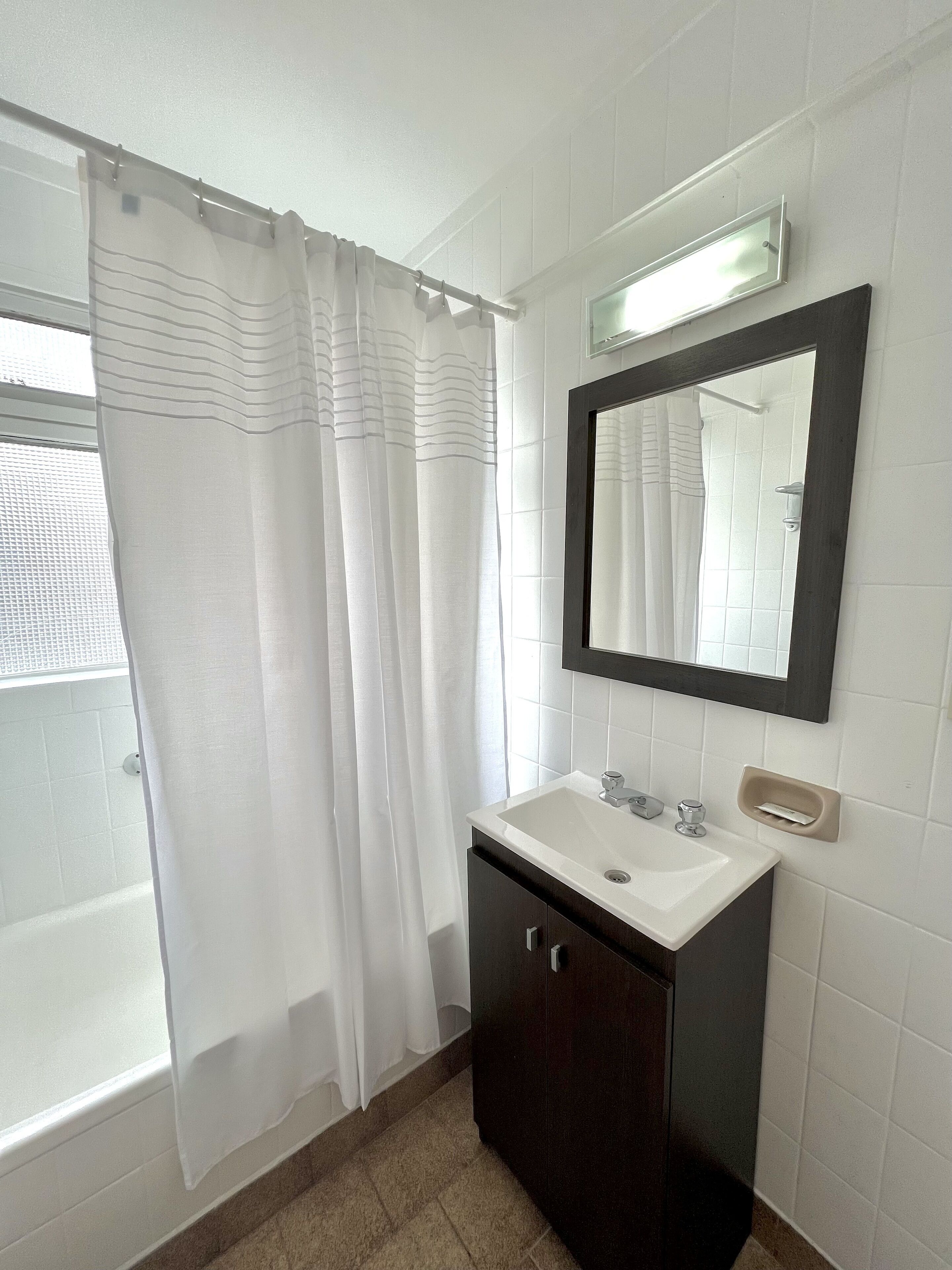 A bathroom with a white sink, dark cabinet, and a mirror above it.