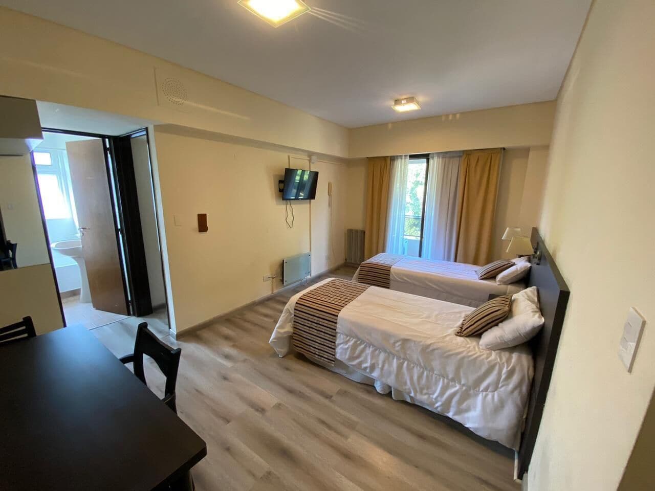 A hotel room with two beds, a dining table, and a TV.
